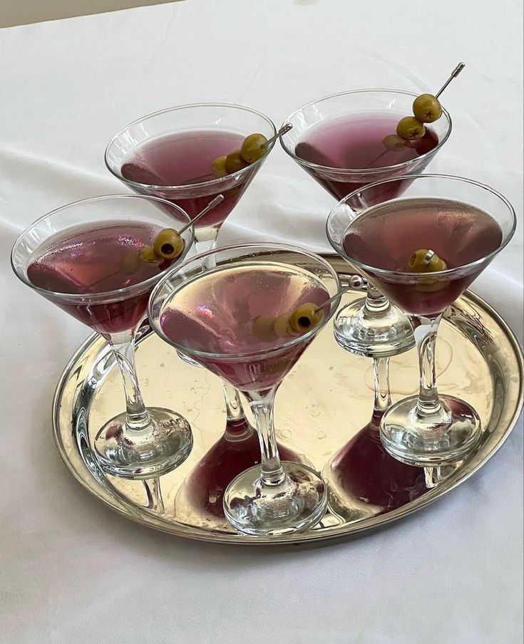 four martini glasses with olives in them on a silver tray