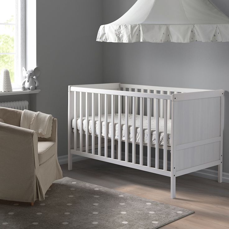 a baby's room with a crib, chair and lamp in the corner