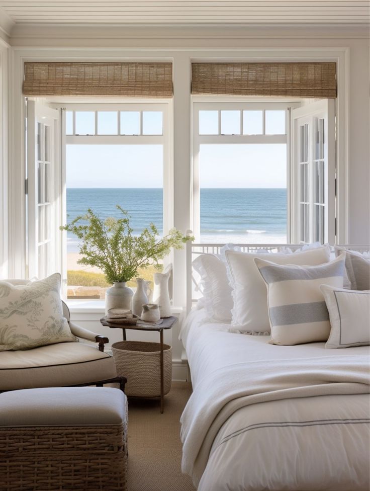 a bedroom with white walls and windows overlooking the ocean is decorated in neutral colors, along with wicker furniture