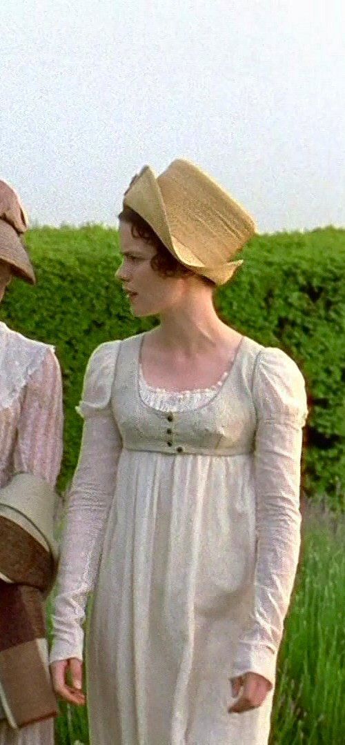 two women in dresses and hats standing next to each other on a field with green grass