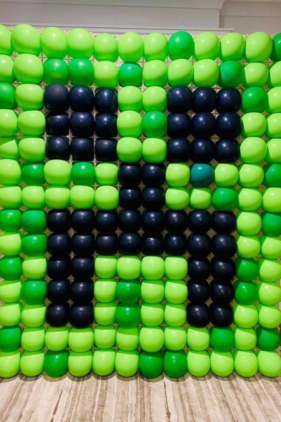 a large green and black letter made out of balloons on top of a wooden floor