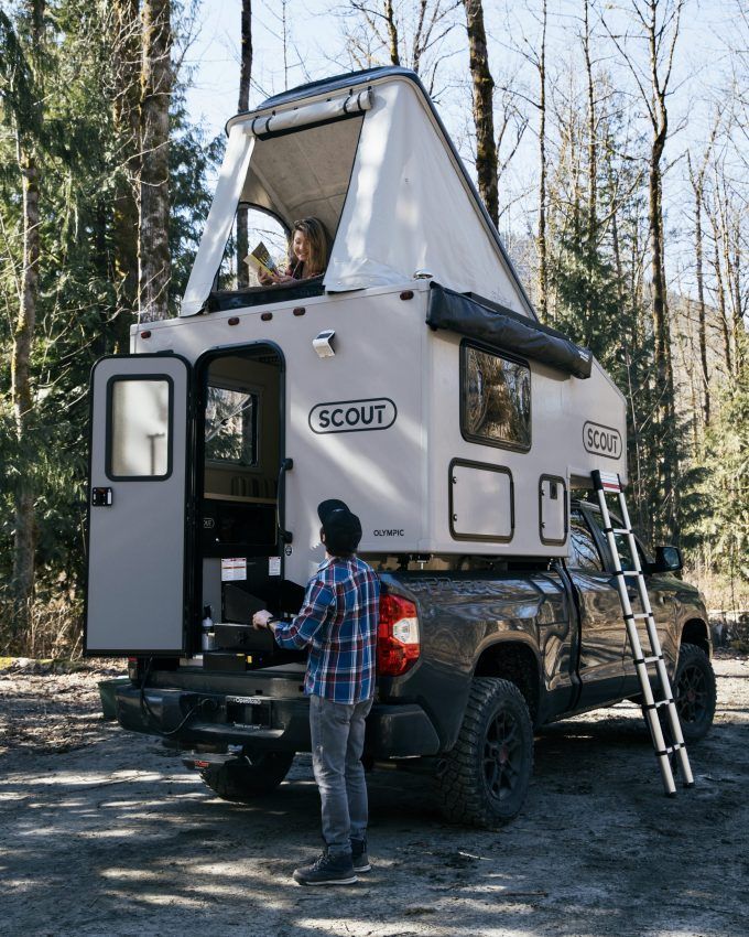 a man standing in the back of a truck next to a white camper trailer