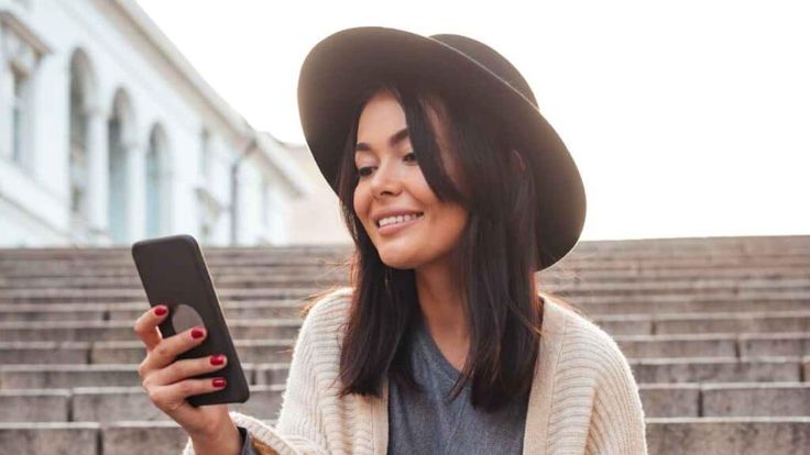 a woman wearing a hat and holding a cell phone in front of some stone steps