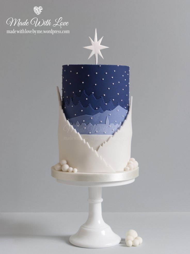 a blue and white cake with stars on top is sitting on a pedestal in front of a gray background