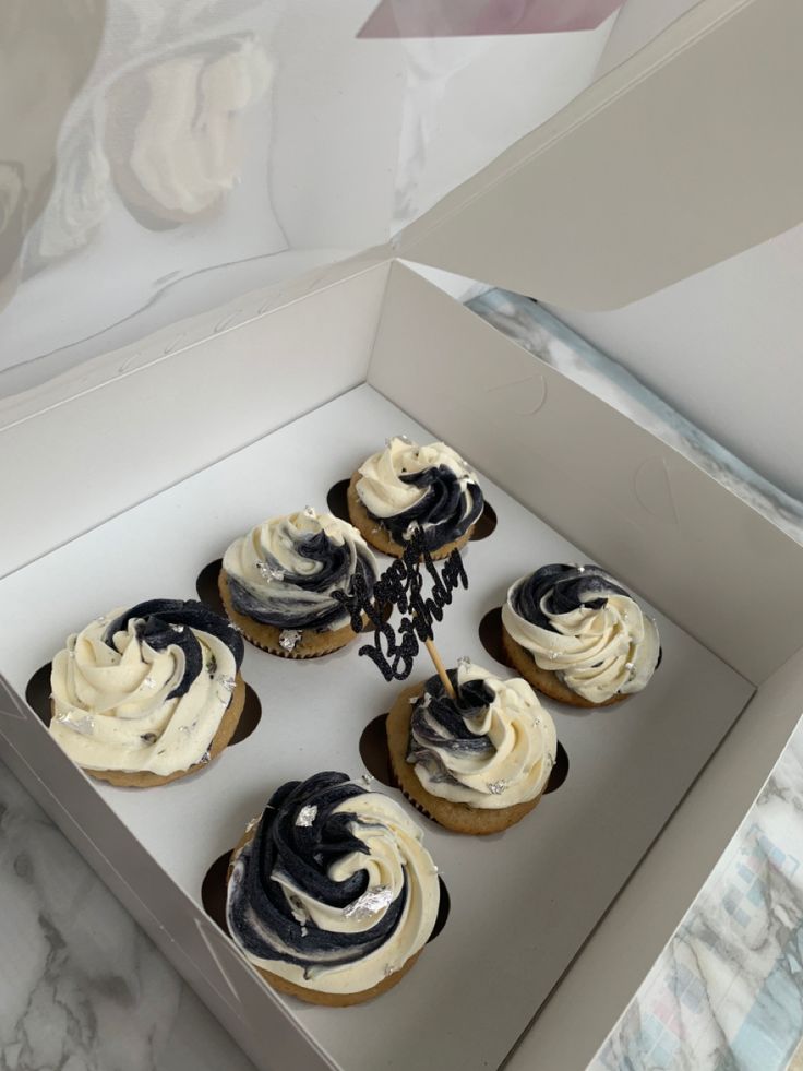 six cupcakes with white frosting and black swirl on top in a box