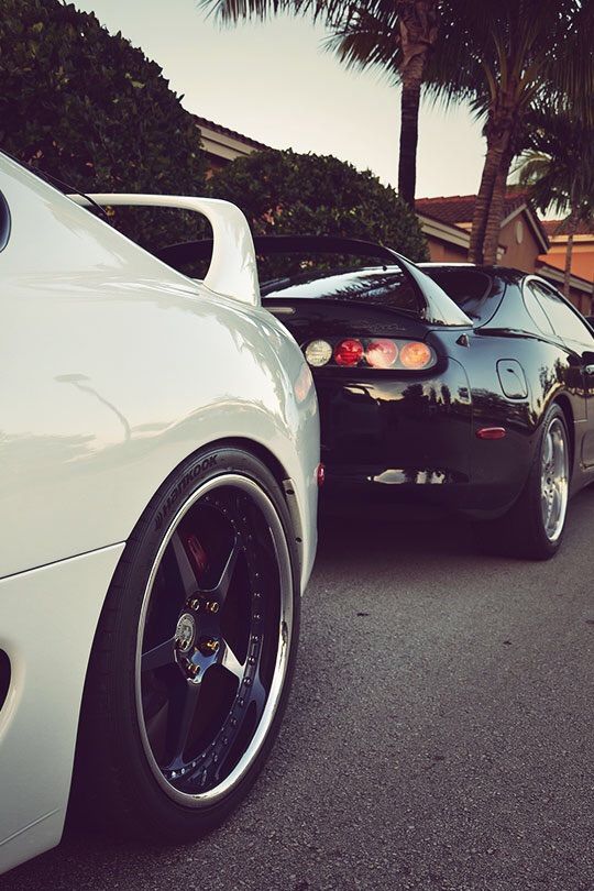 two cars parked next to each other on the side of a road with palm trees in the background