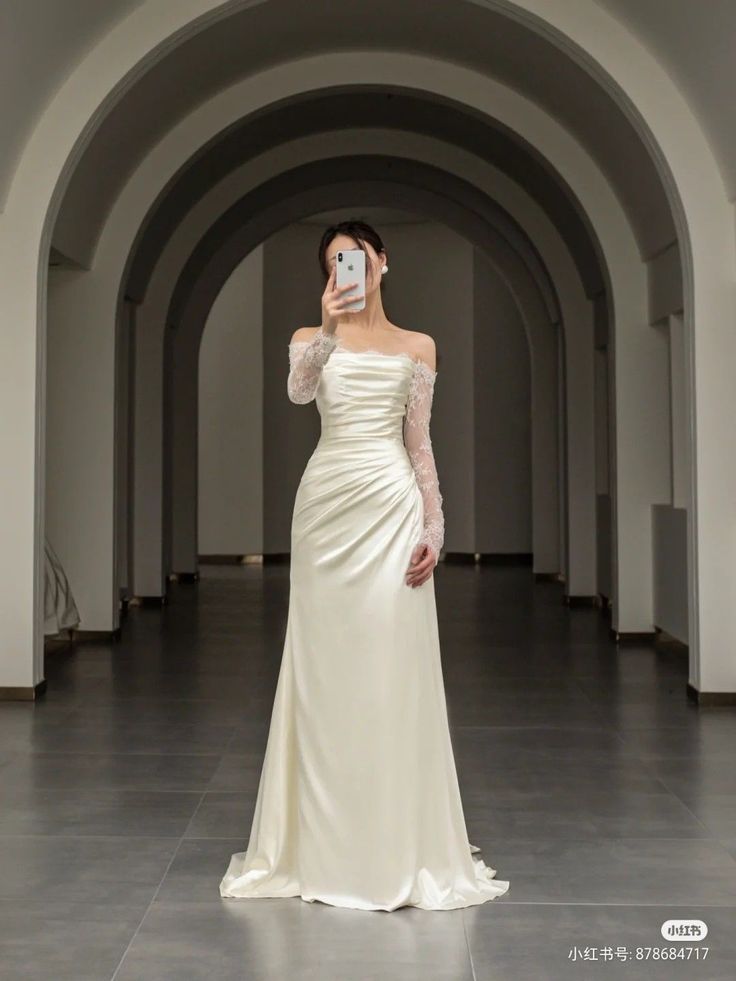 a woman in a white dress taking a selfie with her cell phone while wearing an off the shoulder wedding dress