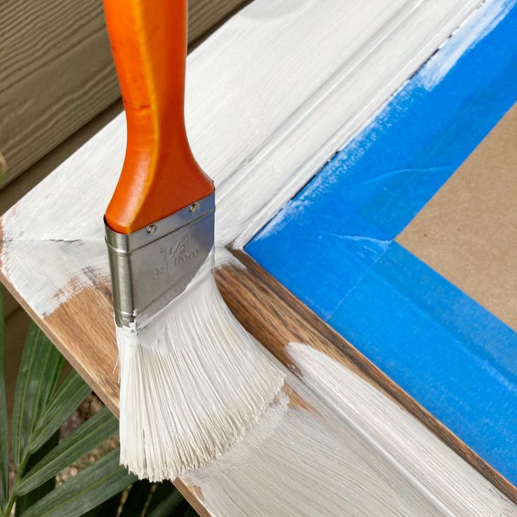 an orange paint brush with white bristles on top of a piece of plywood