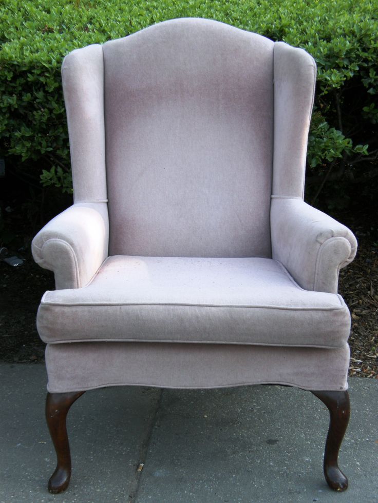 an upholstered chair sitting in front of some bushes