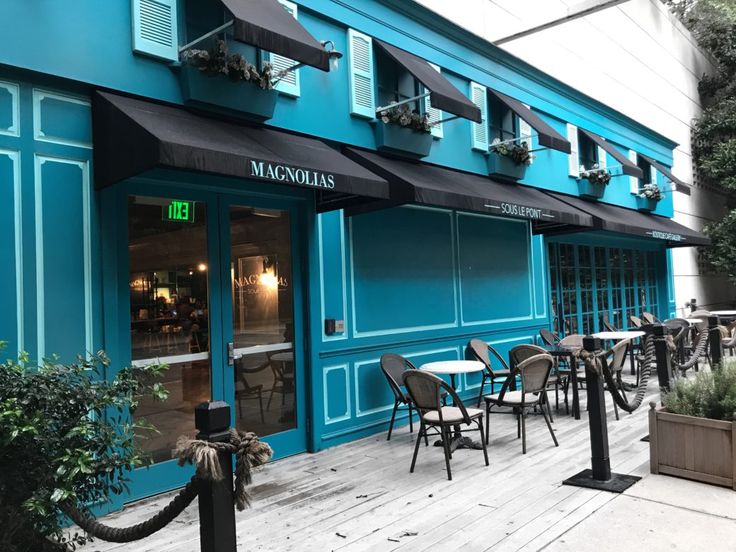 the outside of a restaurant with tables and chairs in front of blue painted walls, windows and doors