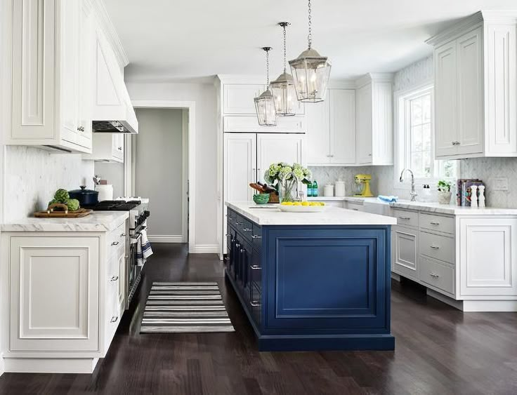 a kitchen with white cabinets and blue island in the center, along with an area rug on the floor