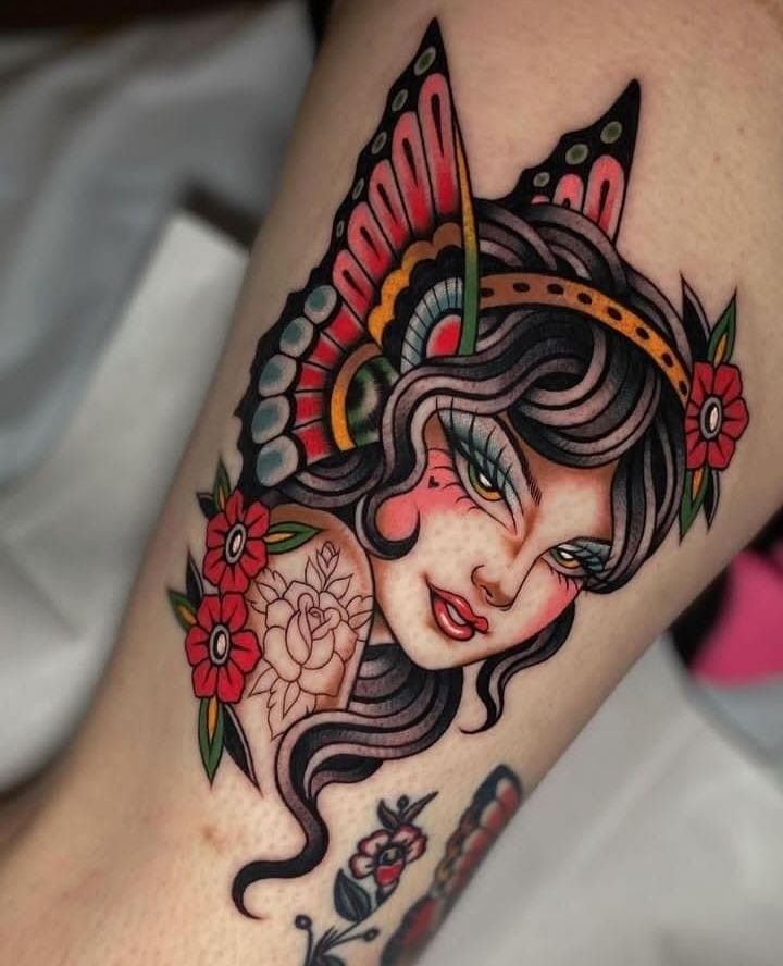 a woman's leg with tattoos on it and flowers in her hair, wearing a headdress