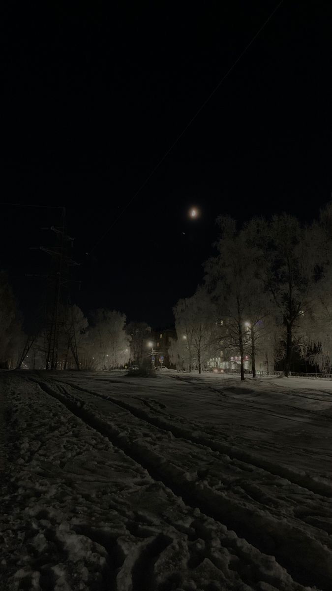 an empty street at night with snow on the ground and power lines in the background