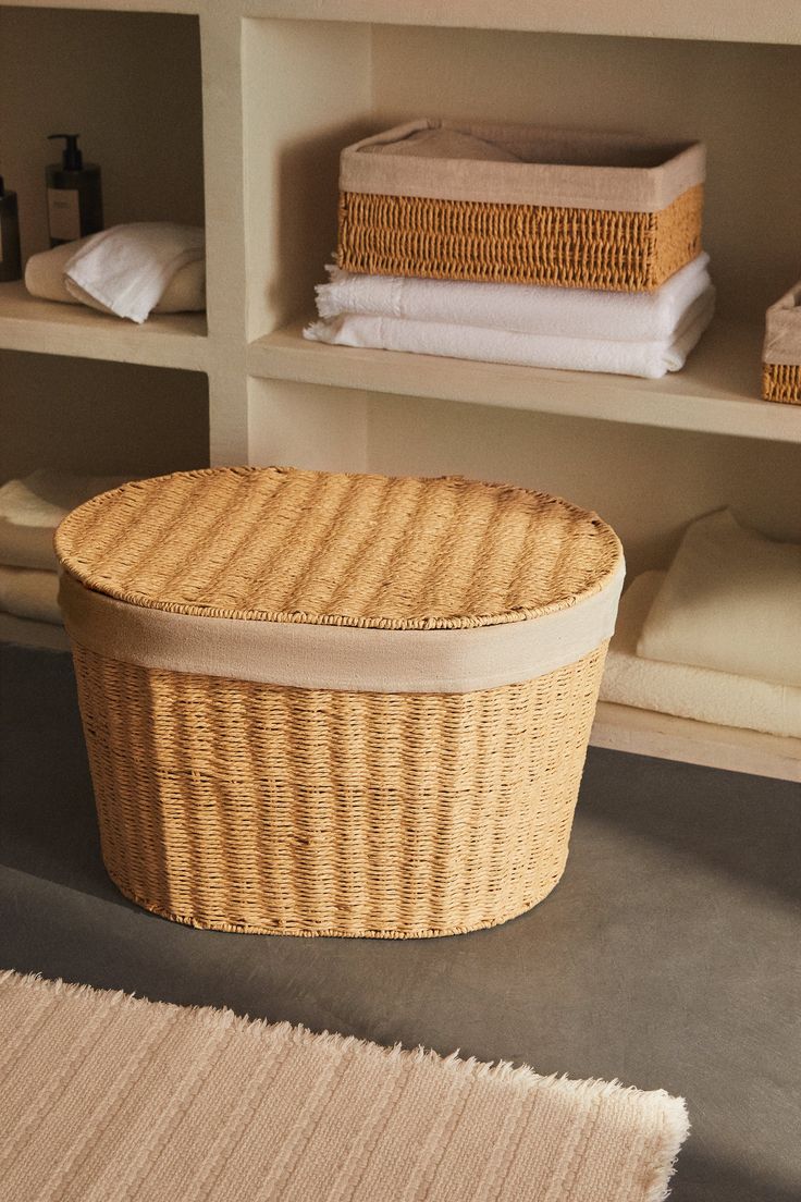 a wicker basket sitting on top of a floor next to shelves filled with folded towels