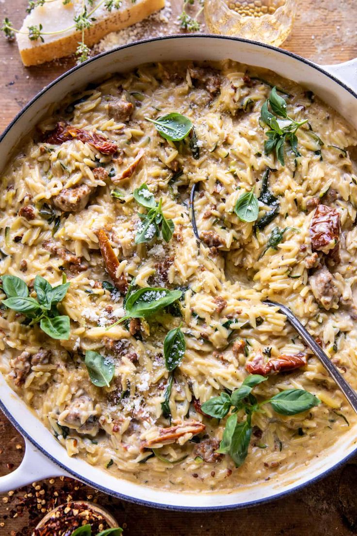 a pan filled with pasta and spinach on top of a wooden table next to bread