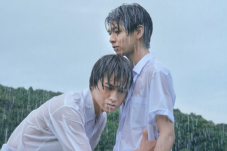 two young men standing next to each other in the rain