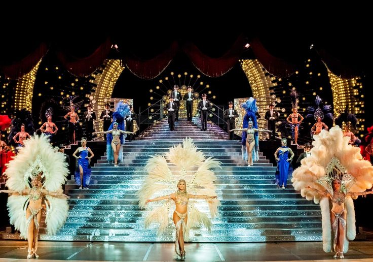 dancers on stage in front of an audience at a show with bright colored costumes and feathers