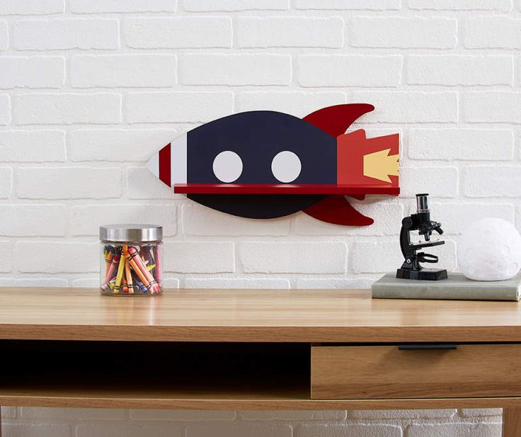 a wooden desk with a red and black rocket ship on it's shelf next to a white brick wall