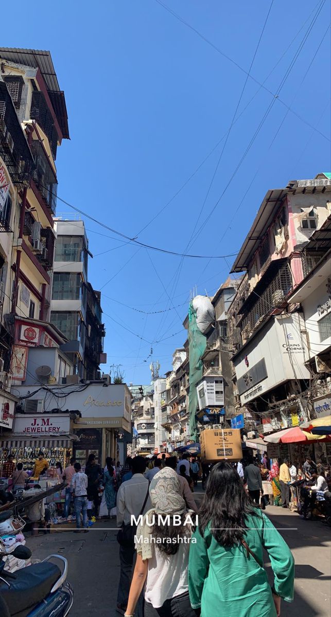 two people walking down the street in front of some shops and buildings with wires above them