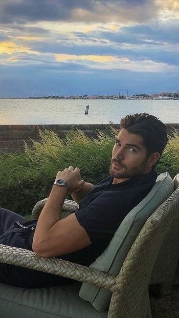 a man sitting on top of a chair next to the ocean with his arms crossed