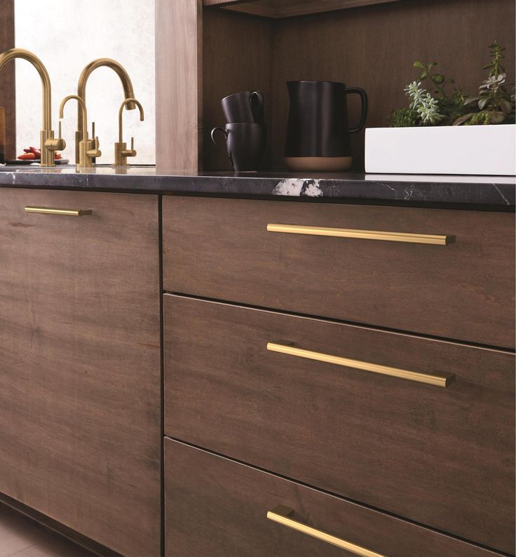 a kitchen with wooden cabinets and black counter tops, gold handles on the faucets