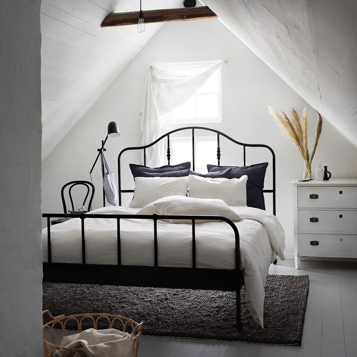 an attic bedroom with white walls and black iron bed frame, rugs on the floor