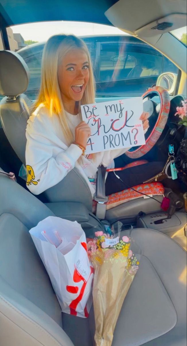 a woman sitting in the back seat of a car holding up a sign that says be my pink prom