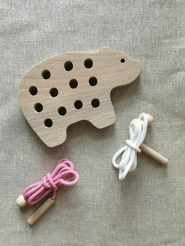 two wooden pegs are next to a pig shaped crafting toy with pink and white yarn