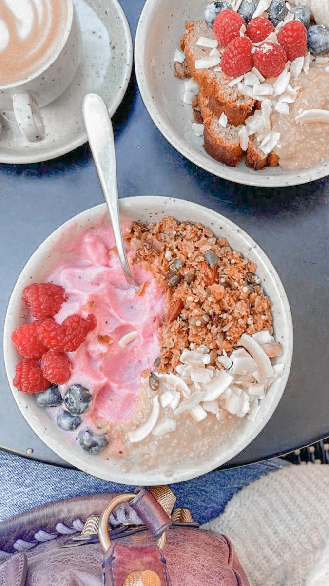 three bowls of food on a table with two cups of coffee and one bowl of granola