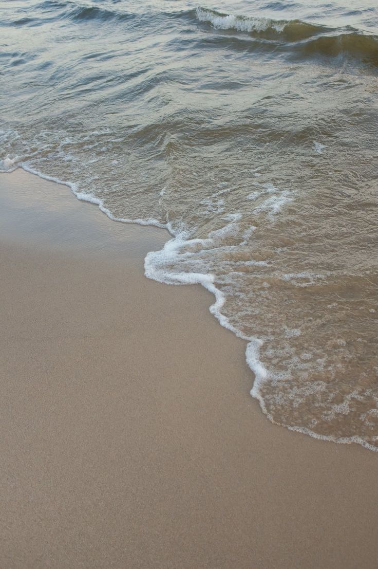 an ocean wave rolls in on the sand at the beach with white foamy waves