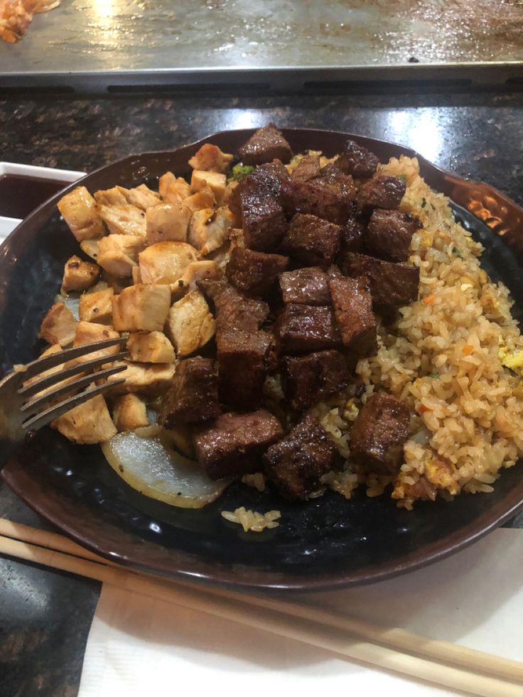 a plate with rice, meat and vegetables next to chopsticks on a table