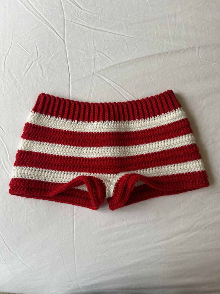 a red and white crocheted shorts laying on top of a bed next to a pillow