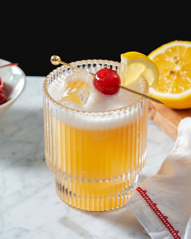 a close up of a drink on a table with lemons and cherries in the background