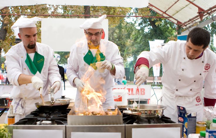 three chefs preparing food on top of a stove in a kitchen area at an outdoor event