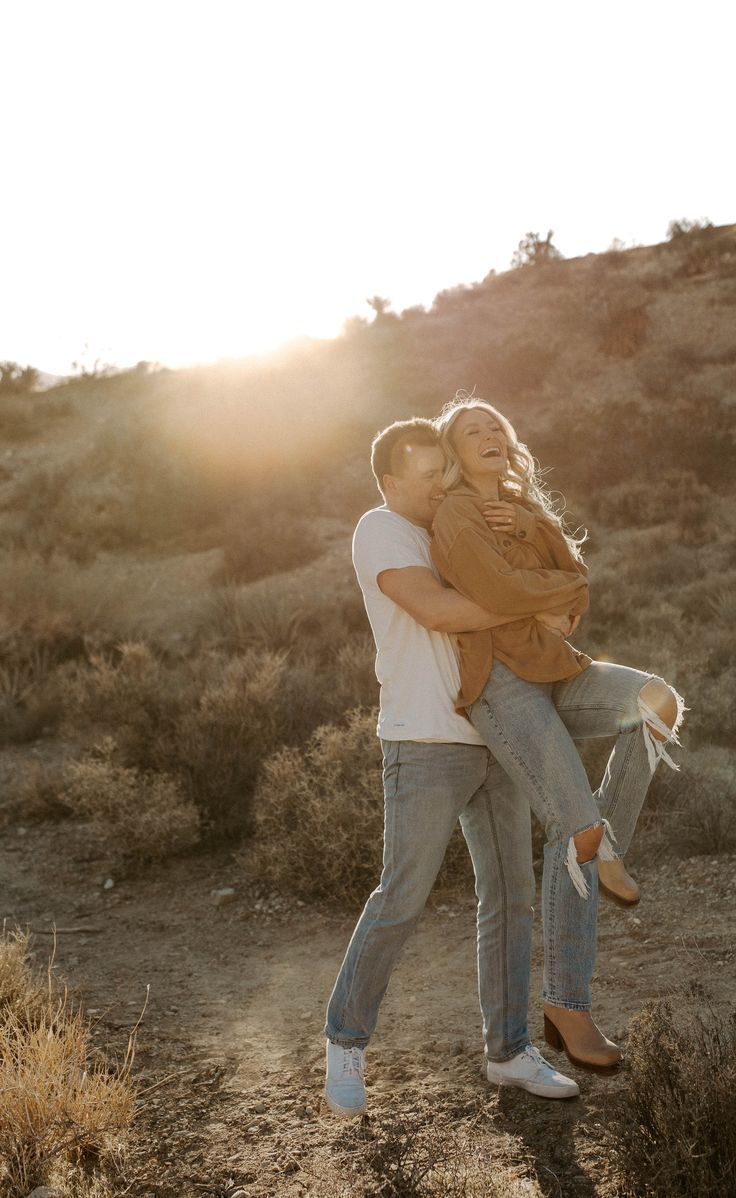 a man carrying a woman on his back in the middle of a desert field at sunset