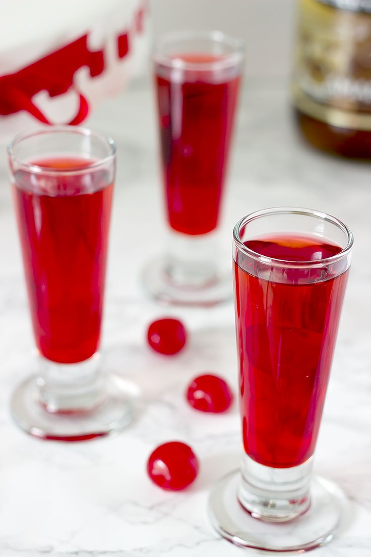 three glasses filled with red liquid sitting on top of a white marble table next to bottles