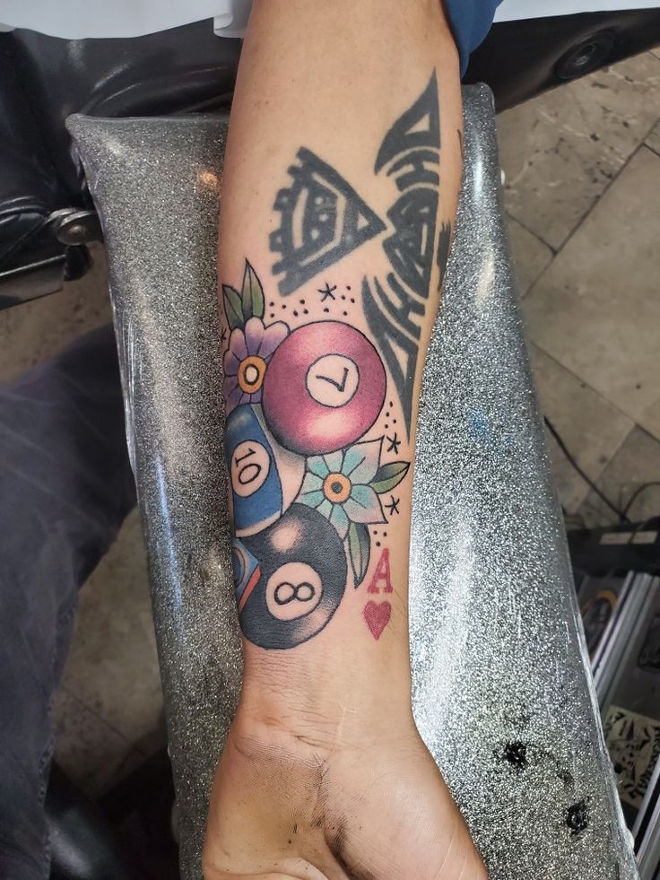 a person with a tattoo on their arm holding up a pool ball and two billiards