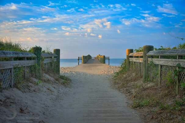 a wooden walkway leading to the beach and ocean with blue skies in the background at sunset