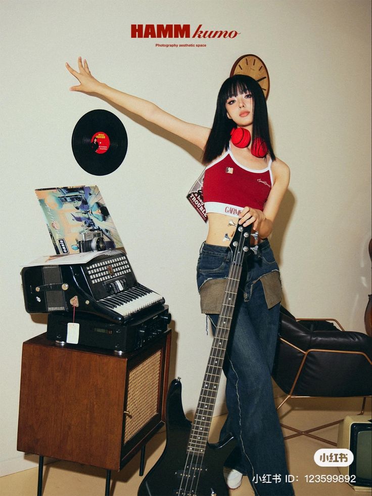 a woman holding a guitar in her right hand and standing next to a record player