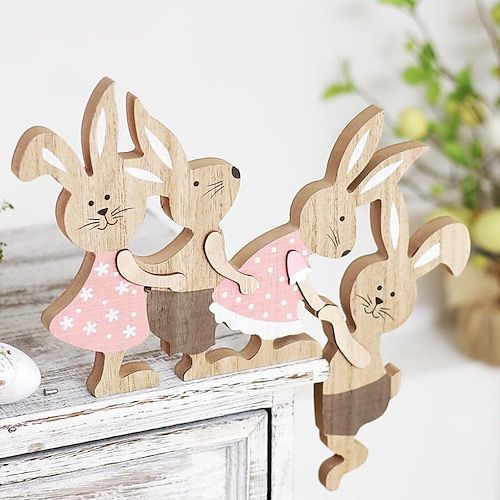 two wooden rabbits standing next to each other on top of a white table with flowers in the background