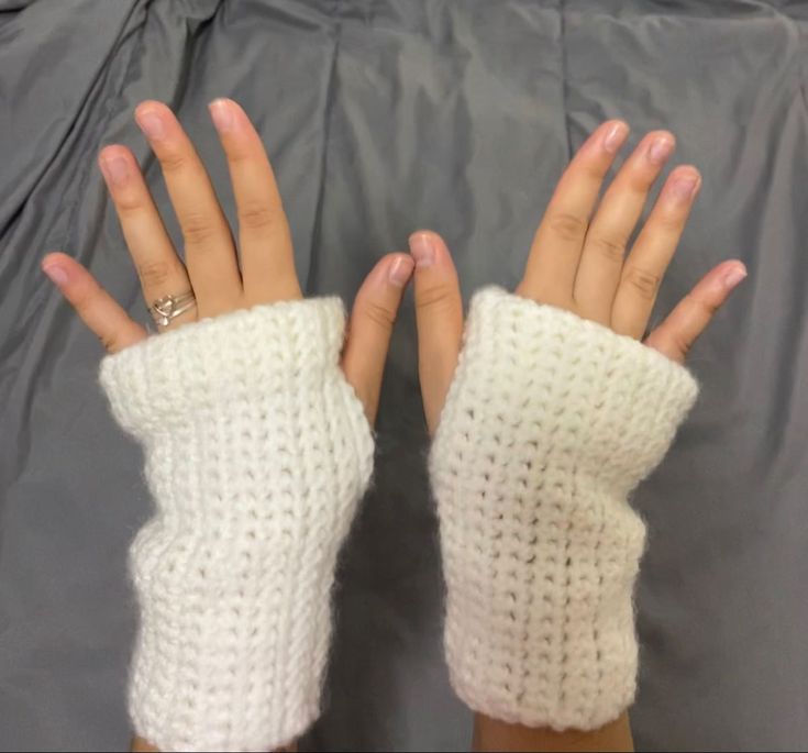 two hands wearing white knitted gloves on top of a gray sheet with one hand in the air