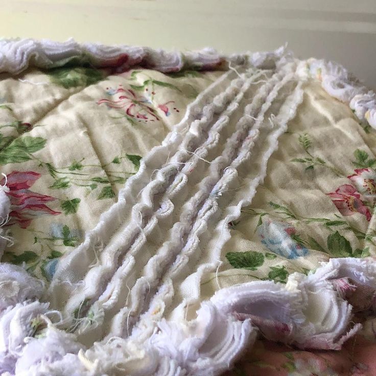 an old blanket with ruffles and flowers on it sitting on top of a bed