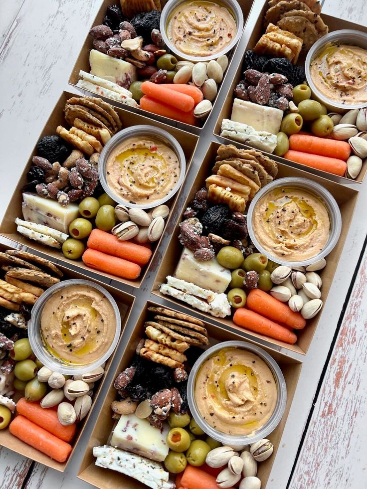 a box filled with different types of food on top of a white wooden table next to carrots and crackers