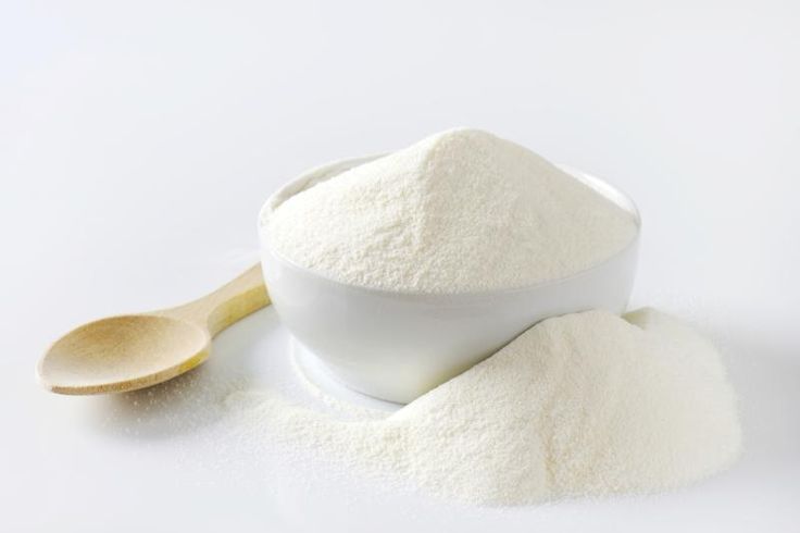 white powder in a bowl and wooden spoon on a white surface with a light colored background