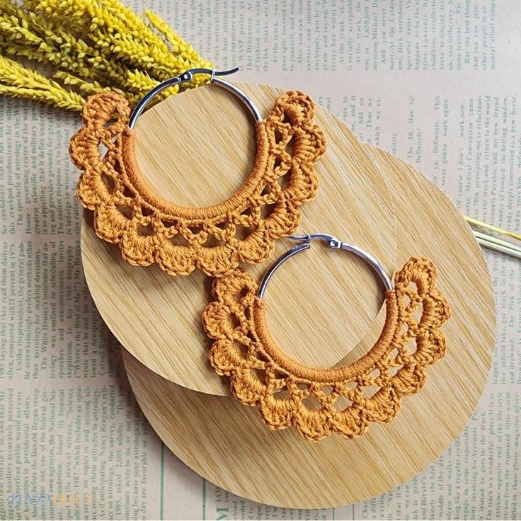 two pairs of wooden hoop earrings with crochet details on top of a book