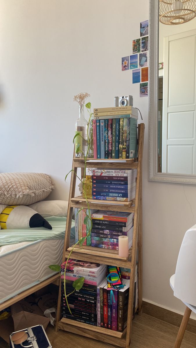 a book shelf with books on it next to a bed and a mirror in the corner