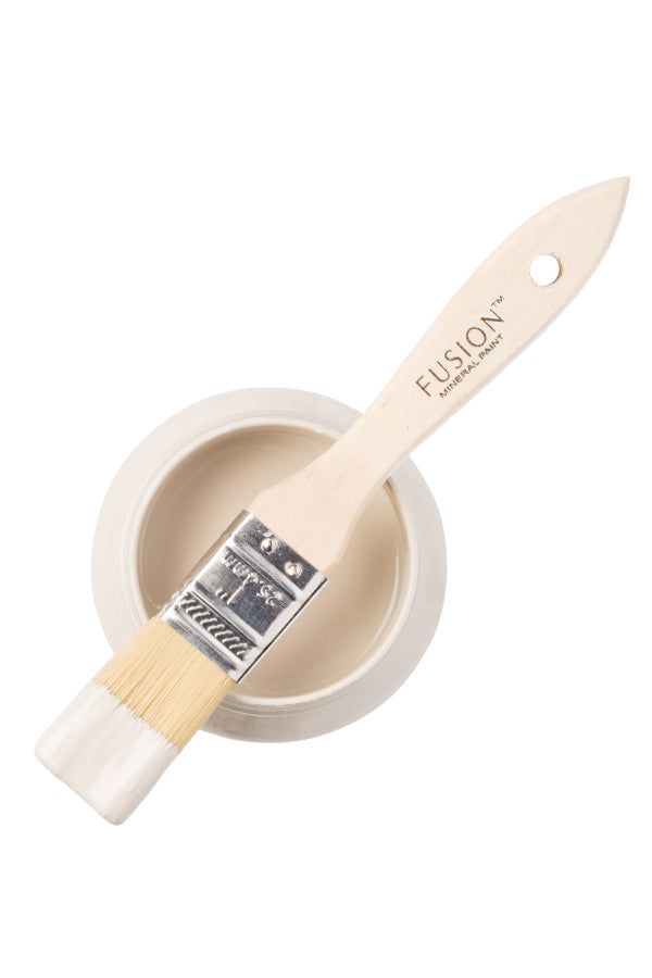 a paint brush sitting inside of a white cup on top of a wooden spoon with the word fusion written on it