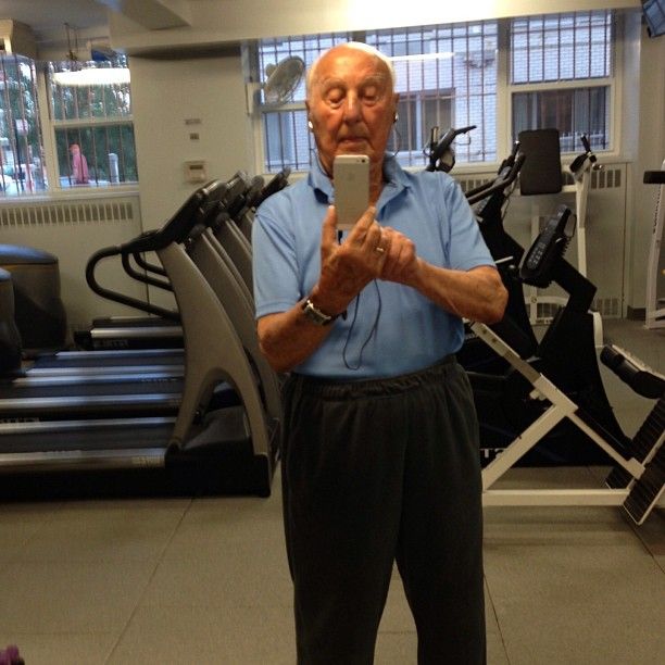 an older man taking a selfie with his cell phone in front of the gym equipment