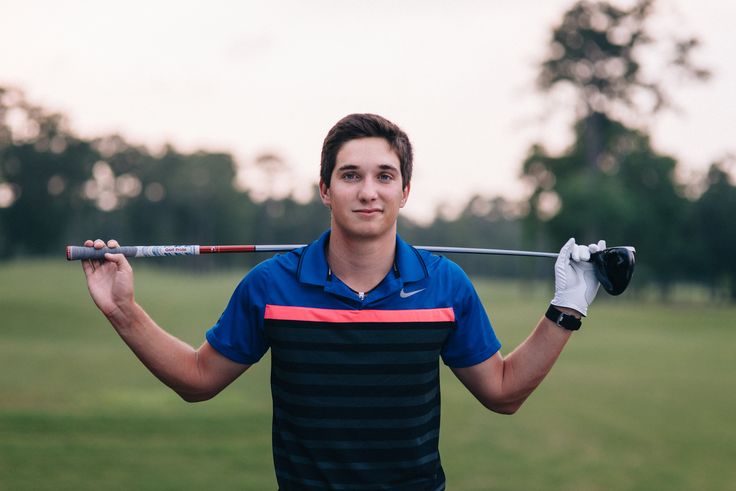 a young man holding a golf club in one hand and wearing a glove on the other