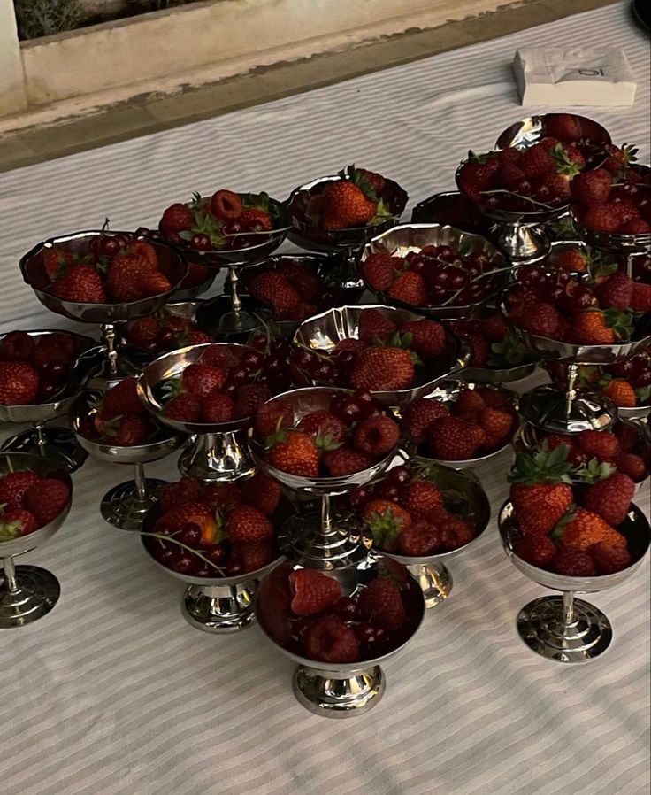 a table topped with lots of silver bowls filled with strawberries on top of each other